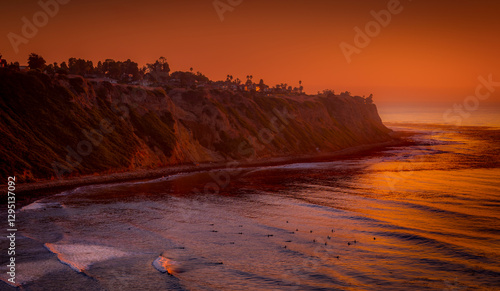 Obraz na płótnie Bluff Cove, Palos Verdes Estates, surfers below wait for the next wave as the sky gives off dramatic hues of red and orange w salonie