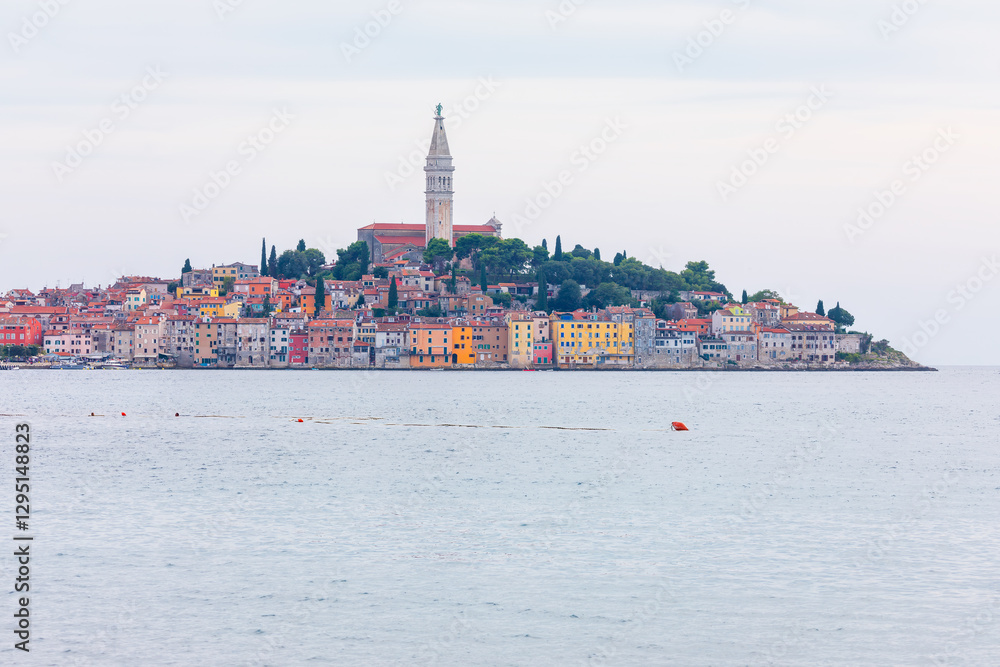 Coastal town of Rovinj Croatia, stands elegantly on peninsula, with colorful buildings rising toward iconic St. Euphemia Church. Calm Adriatic Sea enhances serene beauty of historic Mediterranean gem