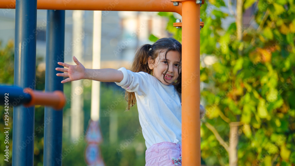 Fototapeta premium A cute little girl child joyfully playing in a children's park surrounded by trees on a fall day