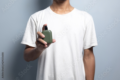 A man wearing a white t-shirt holds a bottle of perfume and sprays it on the front area.