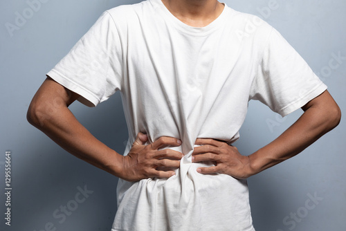 A man wearing a white t-shirt is holding his stomach and seems to be feeling pain in his stomach.