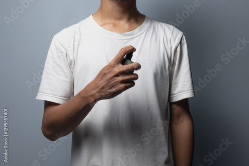 A man wearing a white t-shirt holds a bottle of perfume and sprays it on his body area.