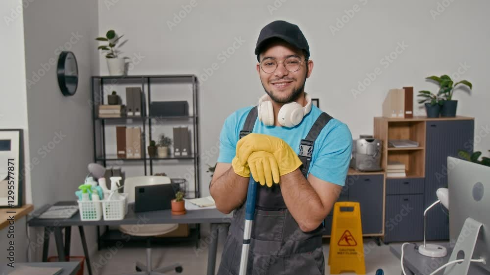 Portrait of cheerful intercultural gen Z male cleaner in uniform and protective gloves looking at camera at modern office Portrait of cheerful intercultural gen Z male cleaner in uniform and protective gloves looking at camera at modern office