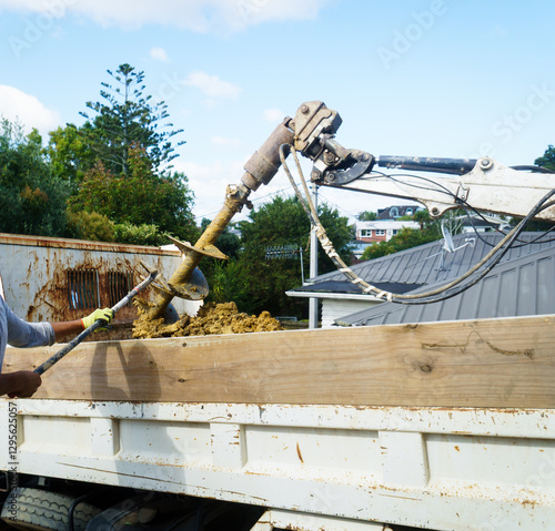 Digging machine loading excavated soil to the truck. Hands of a worker with spade to clean the digger.