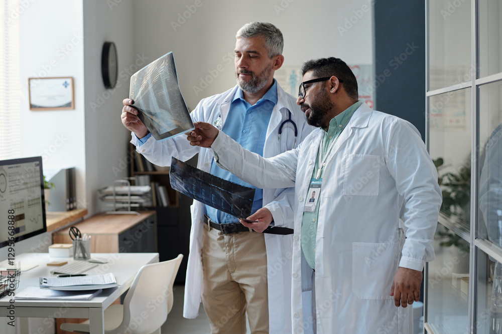 Obraz premium Side view portrait of two mature doctors holding X-ray images and discussing medical case results while standing in clinic office copy space