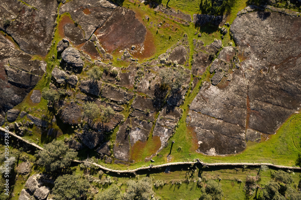 Aerial top-down view of rocky terrain with green vegetation and stone walls in a rural landscape.