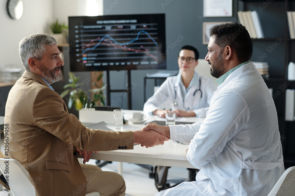 Obraz premium Side view portrait of mature businessman shaking hands with smiling Middle Eastern doctor during medical conference copy space