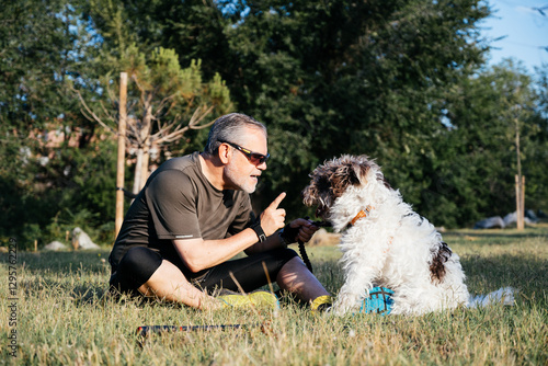 Obraz na plátně Middle-aged Man Instructs Dog During Outdoor Training Session in Sunny Park