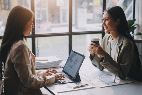 Two young Asian business woman talk, consult, discuss working with new startup project idea presentation analyze plan marketing and investment in the office.