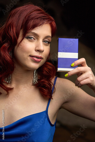 Obraz na płótnie Woman with vibrant red hair holds elegant gift box in blue dress, expressing joy and anticipation, stylish presentation concept w salonie
