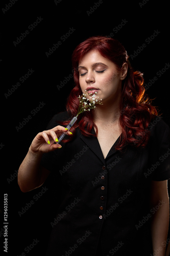 Serene woman with red hair in black dress holding delicate flowers, closing eyes peacefully, embracing tranquility concept