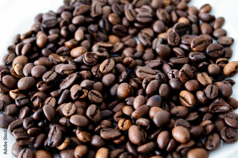 Fototapeta premium Close-up of roasted coffee beans on a white surface, showcasing rich textures and hues.