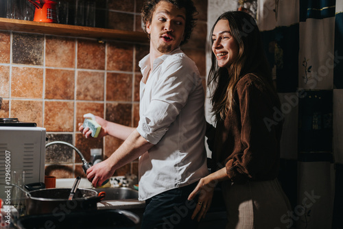 Fotografie A young couple shares playful and joyful interactions while doing household chores in a warm kitchen