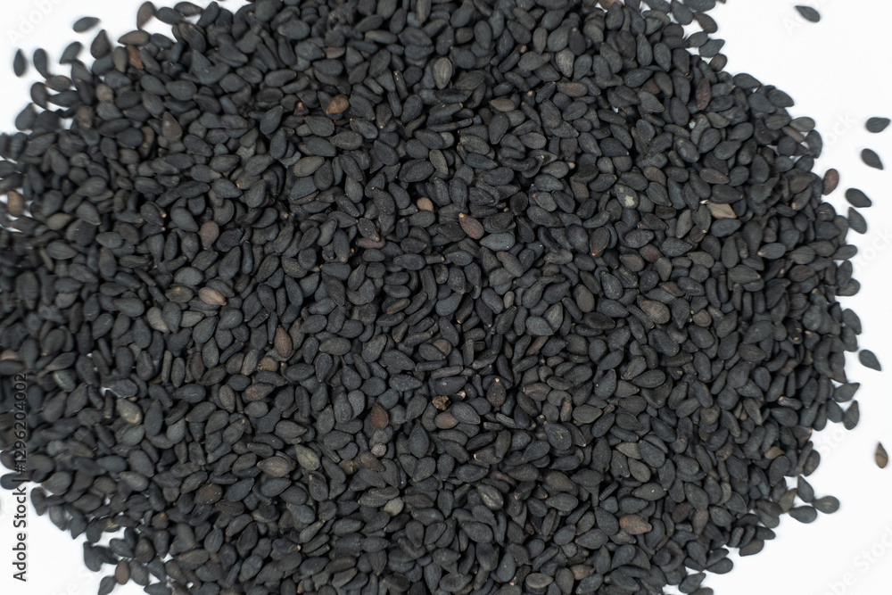 Black sesame seeds scattered on a white background macro top view Black sesame seeds scattered on a white background macro top view