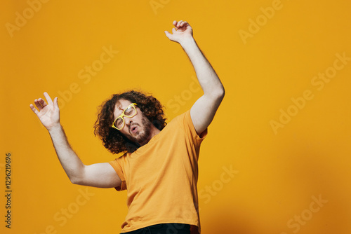 Obraz na plátně Young man dancing joyfully against a vibrant yellow background, wearing quirky y