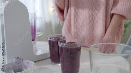 A teenage girl in a pink knitted sweater is pouring a freshly blended berry smoothie into a glass. Healthy nutrition, homemade drinks, and a balanced diet for kids and teenagers.