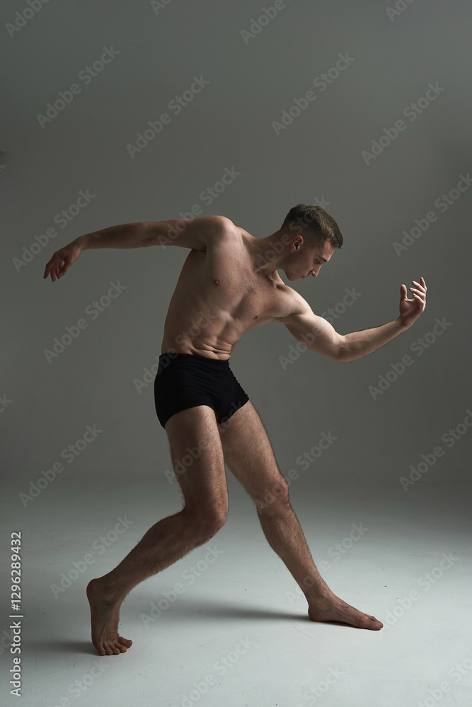 Obraz premium Professional male dancer in motion, performing a contemporary artistic pose with controlled movement, strength, and body expression in a studio