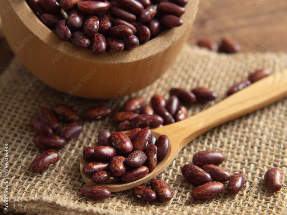 Fototapeta premium Red kidney beans in a scoop on a wooden table against a white background.