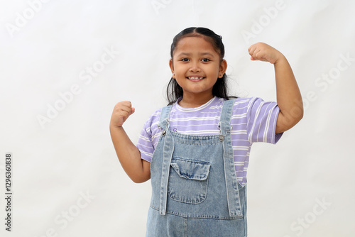 Happy asian little girl standing while showing strong hand gesture. Isolated on white background