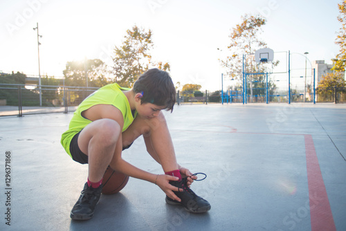 Wallpaper Mural Boy tying his shoe on an outdoor basketball court at sunset. Torontodigital.ca