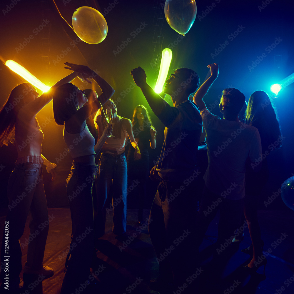 Fototapeta premium Lively group of young friends dancing, enjoying neon-lit party, filled with laughter and vibrant energy. Colorful lights create festive atmosphere, reflecting the carefree joy of youth and connection.