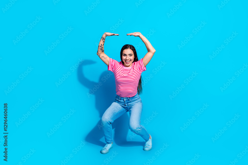 Obraz premium Happy young woman in casual striped outfit posing against a bright blue background, showcasing a joyful attitude