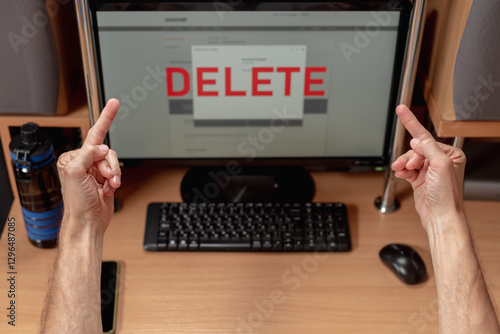 Rude angry man showing two middle fingers to computer screen with text delete, Male user reacting with anger as data deletion occurs on screen, account removal in progress