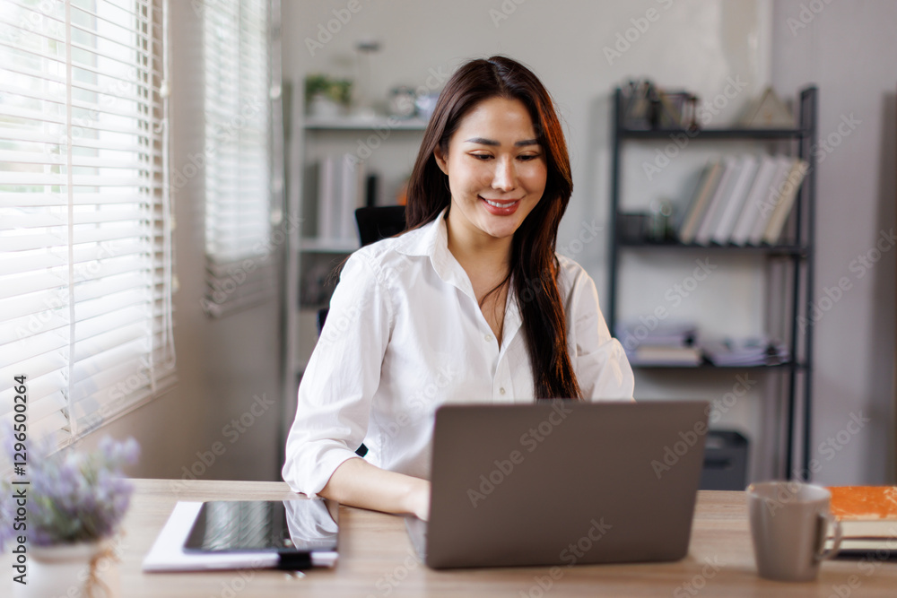 Portrait of asian woman accountant smiles while analyzing financial data on her laptop and using a calculator in a bright office setting
