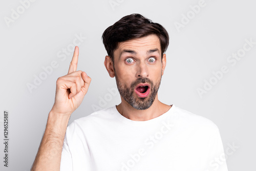 Foto Surprised young man with beard pointing upward in a white T-shirt, expressing ex