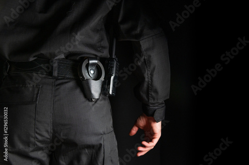 security guard controlling the premises. bodyguard in black uniform on black background, with handcuffs on his belt