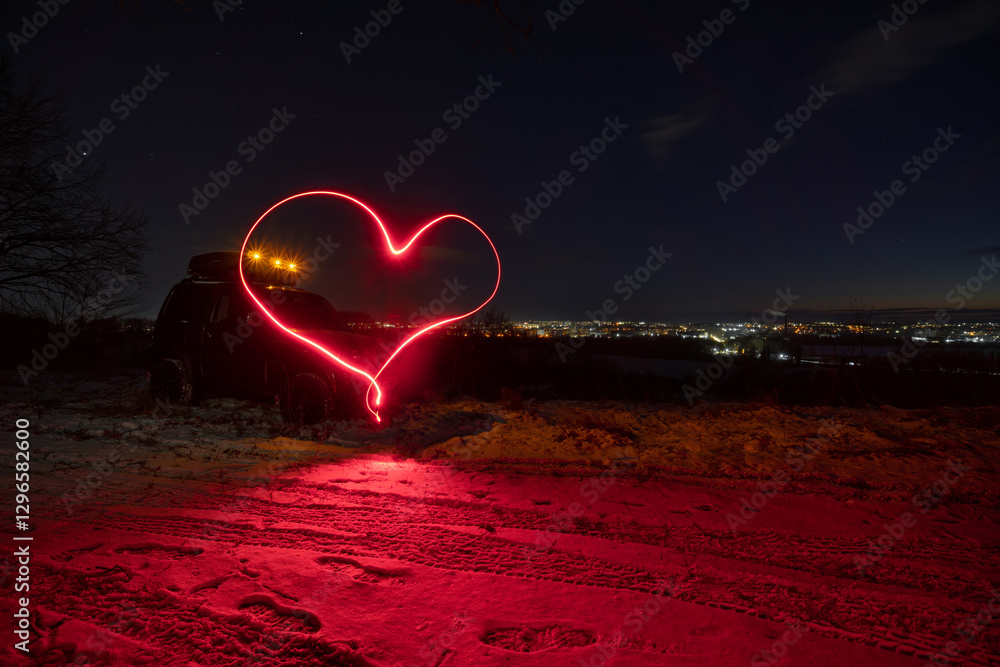 an old all-terrain vehicle stands on the top of the mount, In the background are the lights of the city, a late sunset on a winter evening. A heart is drawn with long exposure light