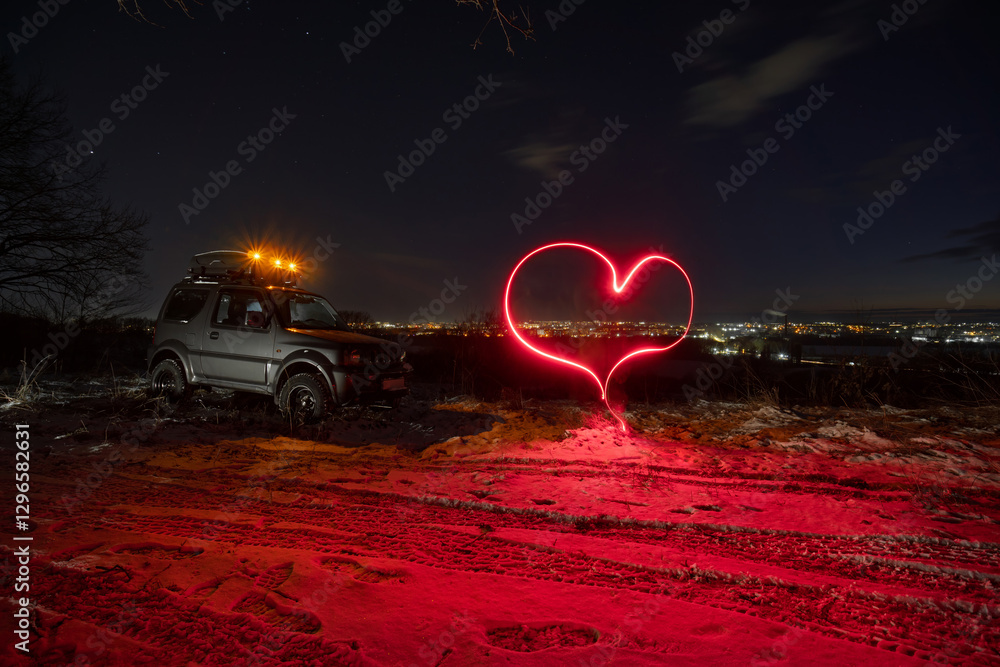 an old all-terrain vehicle stands on the top of the mount, In the background are the lights of the city, a late sunset on a winter evening. A heart is drawn with long exposure light