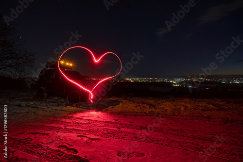 Obraz na płótnie an old all-terrain vehicle stands on the top of the mount, In the background are the lights of the city, a late sunset on a winter evening. A heart is drawn with long exposure light w salonie