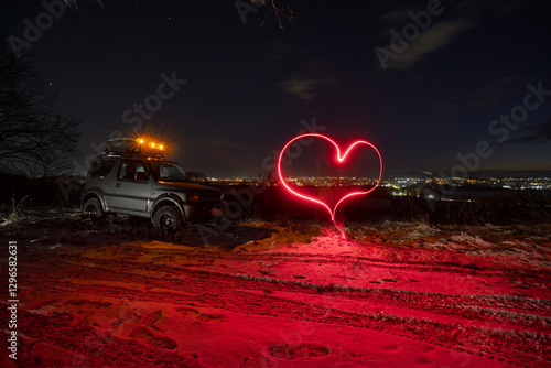 Obraz na płótnie an old all-terrain vehicle stands on the top of the mount, In the background are the lights of the city, a late sunset on a winter evening. A heart is drawn with long exposure light w salonie