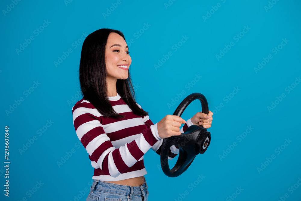 Young happy woman holding steering wheel in striped shirt with blue background Young happy woman holding steering wheel in striped shirt with blue background