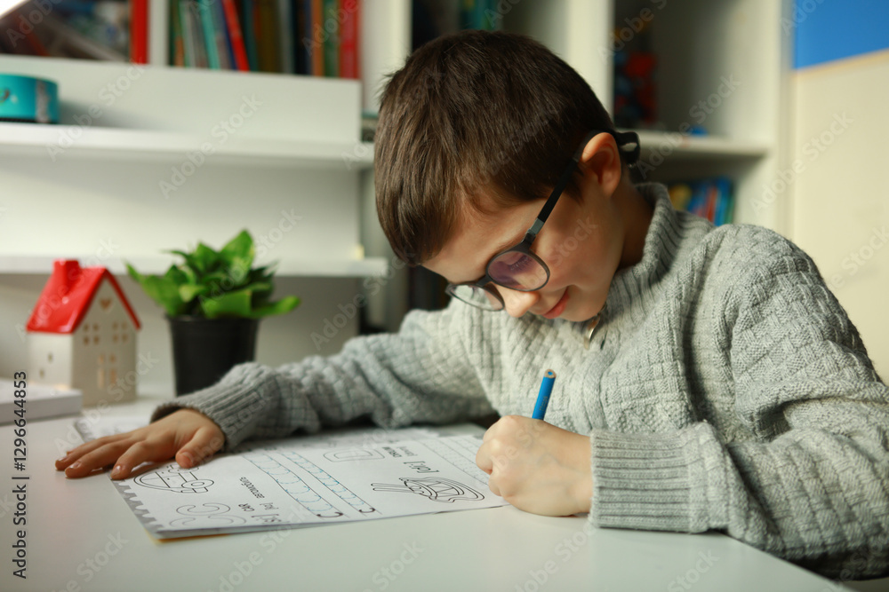 Naklejka premium the boy is learning to write letters.The boy with glasses is doing his homework at home