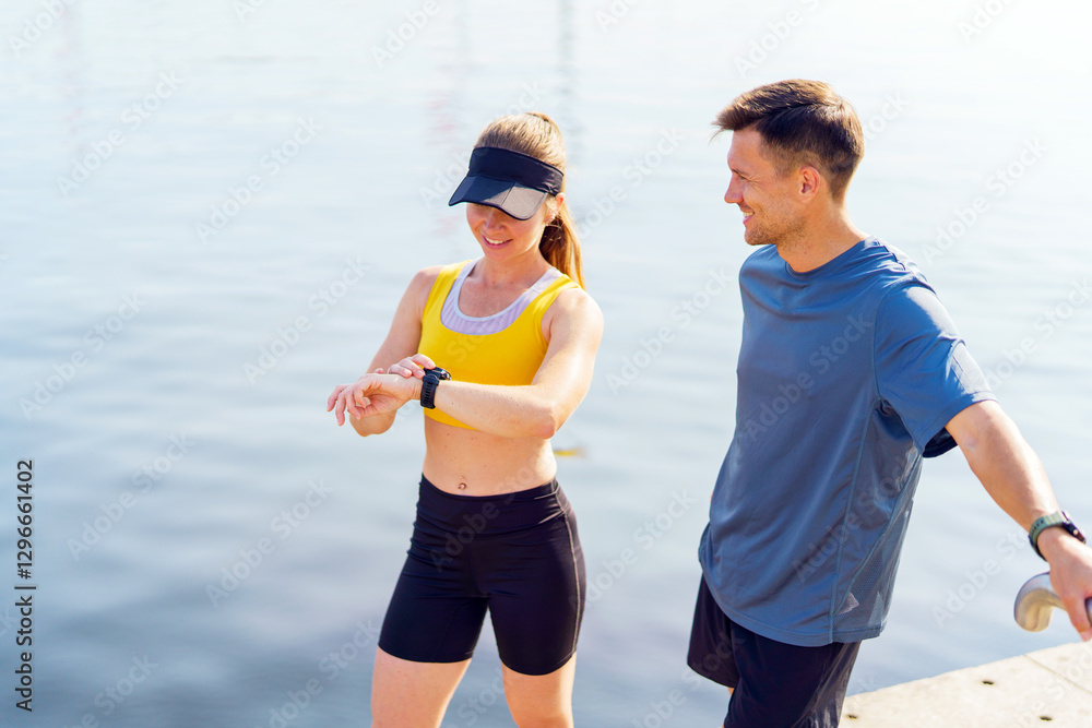 Fototapeta premium Couple enjoys a morning run by the water while checking fitness watch in summer weather
