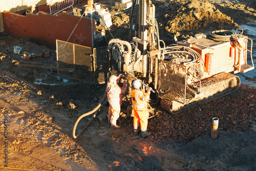 Construction workers repairing heavy drilling machinery at a worksite during sunset