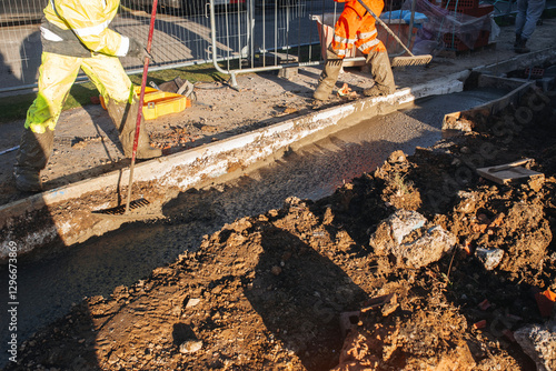 Workers perform construction and concrete pouring along public road during daylight while wearing safety gear for protection in an urban setting photo