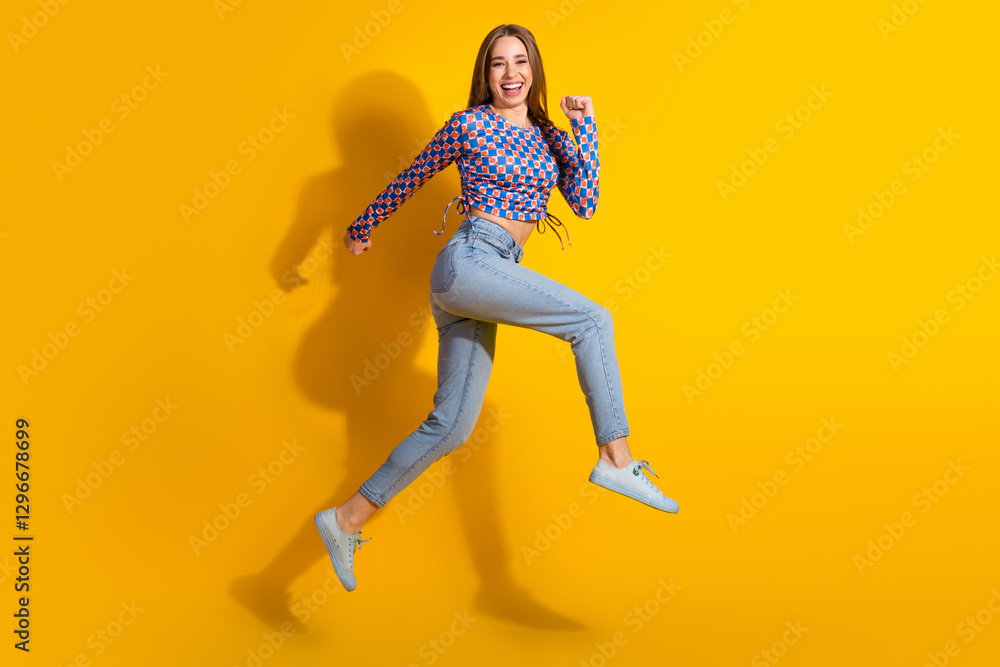 Cheerful young woman in casual jeans and colorful top jumping against yellow background with enthusiasm Cheerful young woman in casual jeans and colorful top jumping against yellow background with enthusiasm