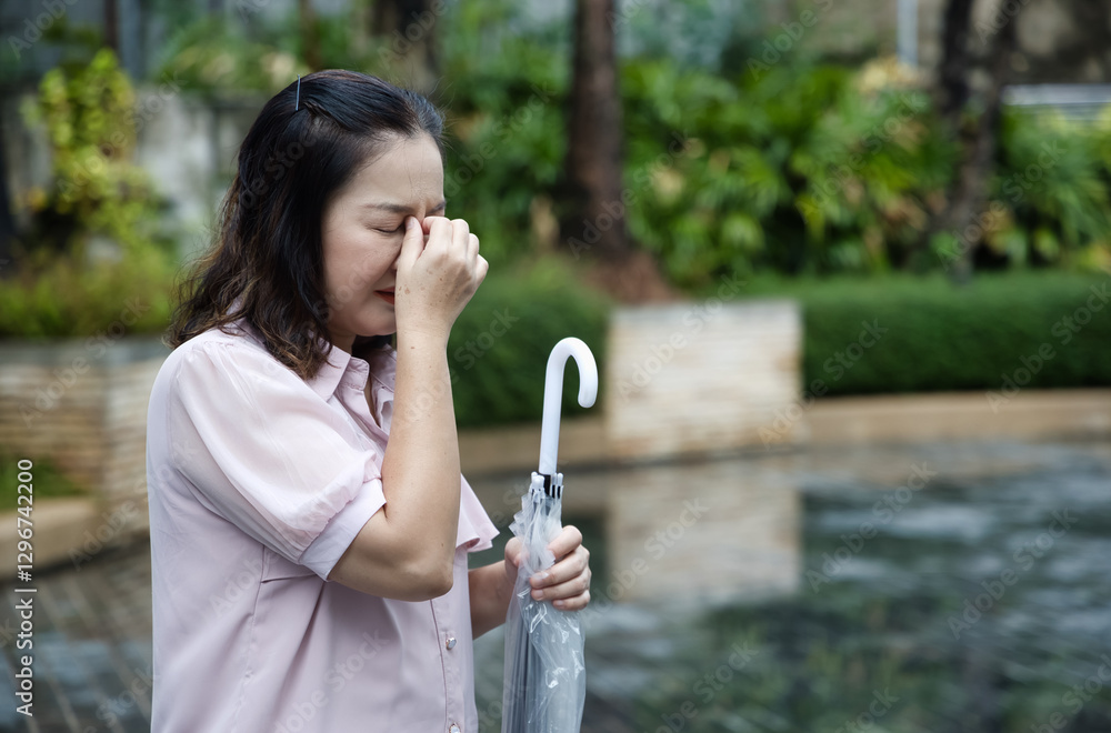 Asian middle-aged woman holding umbrella after raining, sick Asian aunt having cold, flu, fever and headache due to changing weather and rainfall Asian middle-aged woman holding umbrella after raining, sick Asian aunt having cold, flu, fever and headache due to changing weather and rainfall
