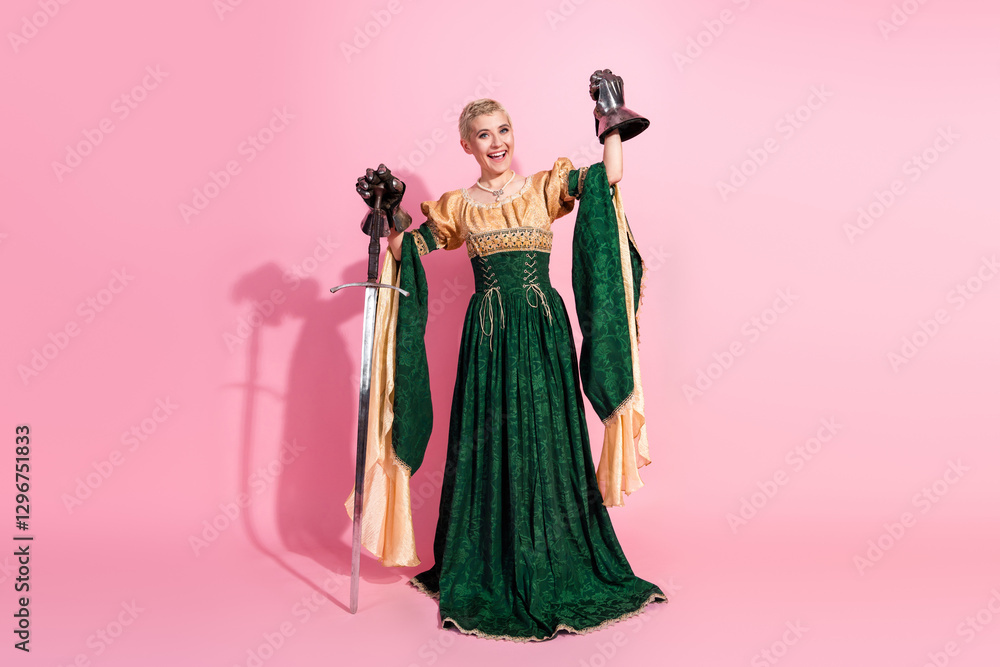 Fototapeta premium Elegant woman in medieval costume holding props and posing on pink studio background