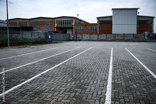 Parcheggio in pavimentazione autobloccante con segnalatica bianca con edificio industriale sullo sfondo