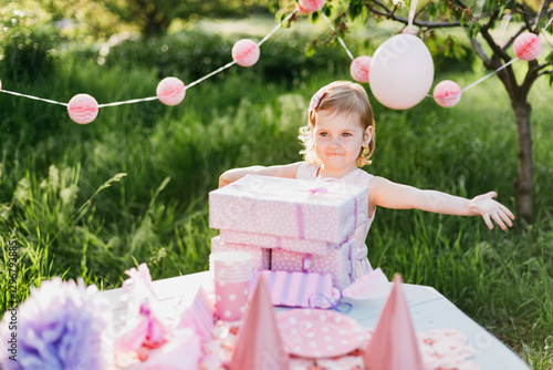 Happy birthday little girl with gift box in beautiful garden. child eat happy birthday rose cupcake. colorful pastel decoration outdoor. 4 years old kid celebrating enjoying party on summer day. photo