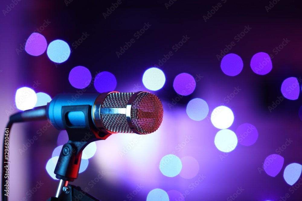 Obraz premium Microphone on stand against color background with blurred lights, space for text. Bokeh effect