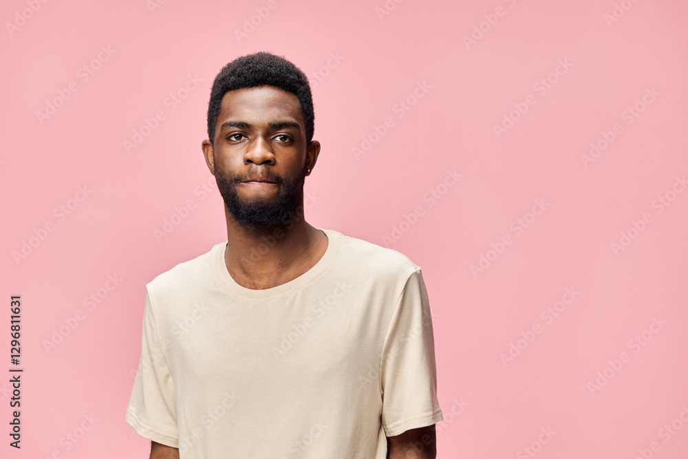 Young African man in a neutral t shirt with a contemplative expression against a pink backdrop, conveying introspection and thoughtfulness, ideal for lifestyle themes Young African man in a neutral t shirt with a contemplative expression against a pink backdrop, conveying introspection and thoughtfulness, ideal for lifestyle themes