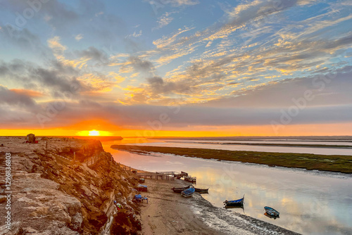 Sunset over the pier and old wooden fishing boats in Naila Lagoon, Morocco