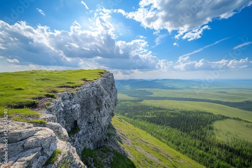 Breathtaking mountain view  rocky outcrop overlooking lush green valley and blue sky with clouds
