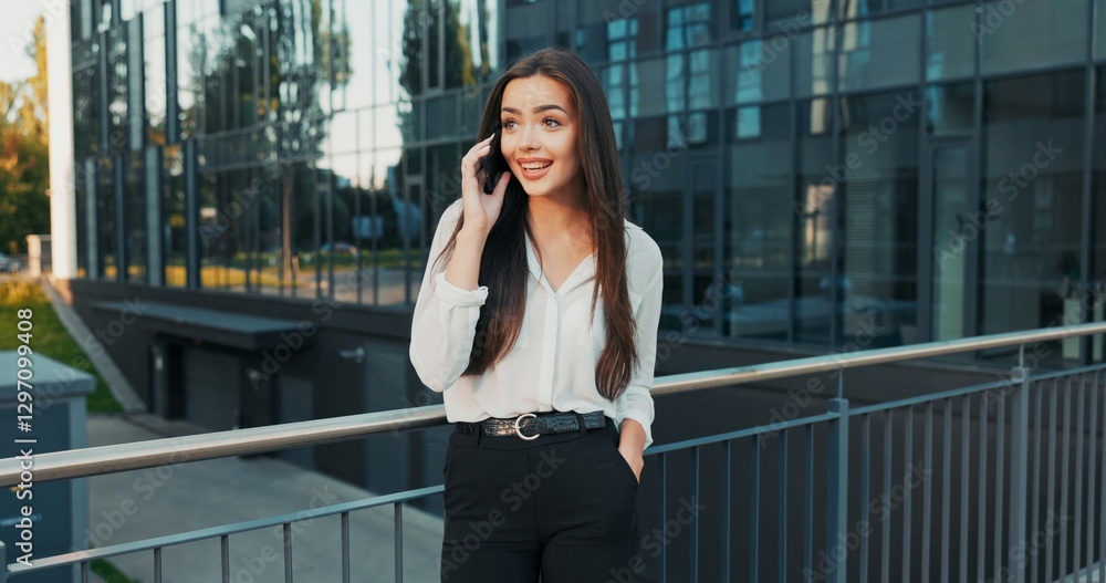 Fototapeta premium Stressed anxious woman in elegant clothes walks out to break in front of glass company building makes call on phone her boss learn good news feels relieved pulls phone away from ear looks up smiling