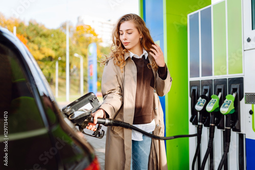 A young woman at a gas station fills up her car with one hand and checks her smartphone with the other. A young driver fills up his car contactlessly on the street. Concept of technology, modernity.